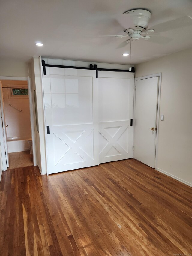 unfurnished bedroom featuring a barn door, wood finished floors, recessed lighting, baseboards, and ceiling fan