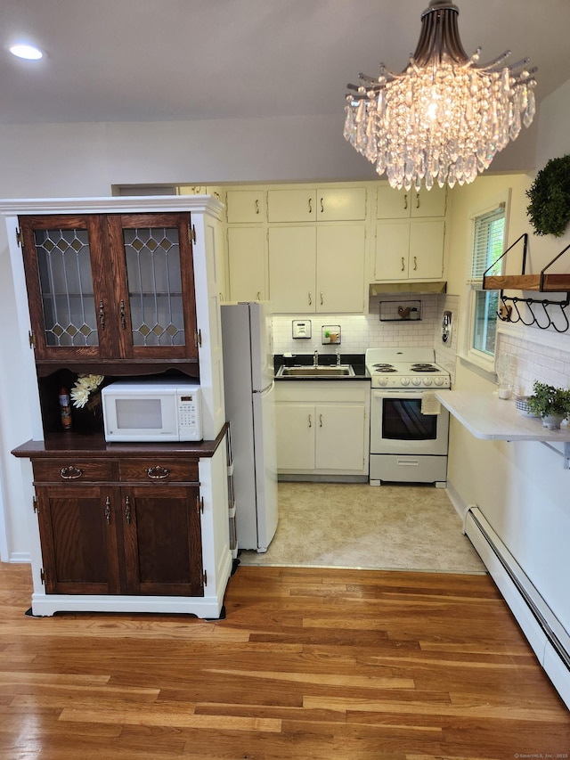 kitchen featuring white appliances, a baseboard radiator, a chandelier, a sink, and tasteful backsplash
