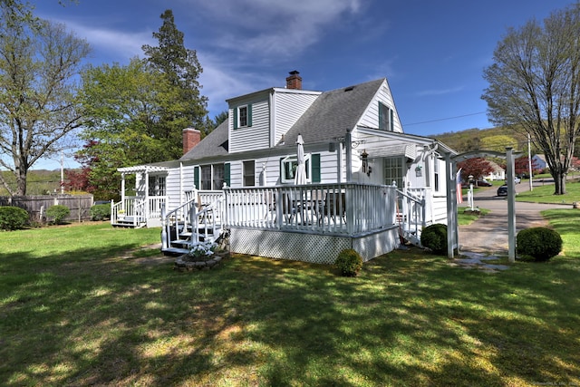 rear view of property with a chimney, a lawn, a wooden deck, fence, and a shingled roof