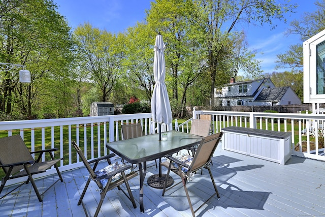 wooden terrace featuring outdoor dining area, a fenced backyard, a yard, a storage shed, and an outbuilding