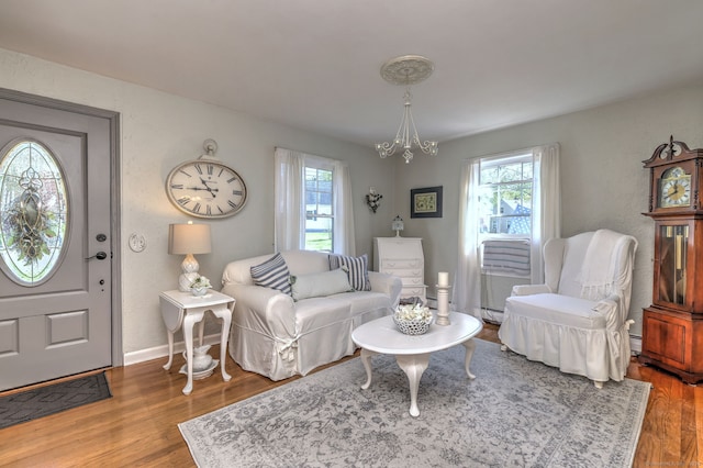 living area with a baseboard heating unit, baseboards, an inviting chandelier, and wood finished floors
