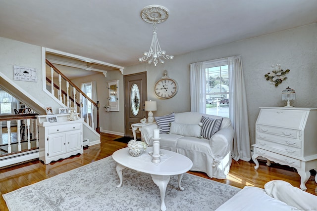 living room featuring an inviting chandelier, dark wood finished floors, baseboard heating, and stairway