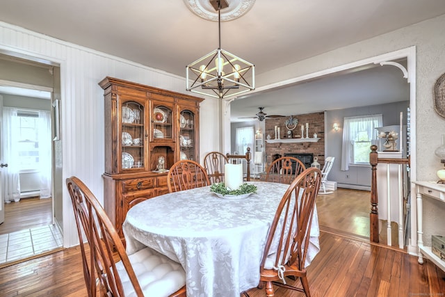dining area with a baseboard heating unit, a fireplace, ceiling fan with notable chandelier, and hardwood / wood-style floors