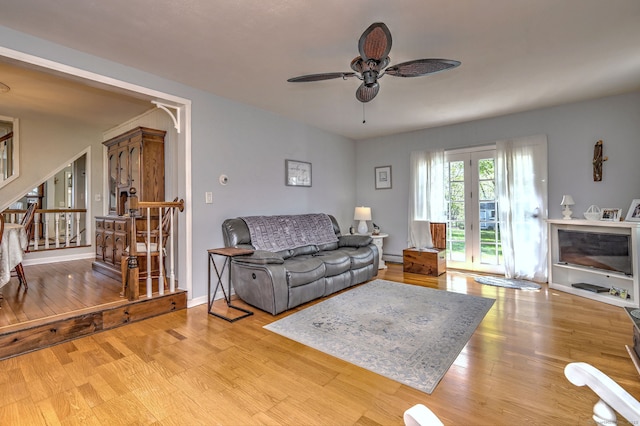 living room featuring stairway, baseboard heating, a ceiling fan, and wood finished floors