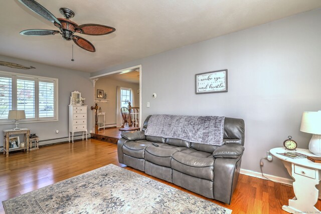 living area featuring baseboard heating, a ceiling fan, baseboards, wood finished floors, and a baseboard heating unit