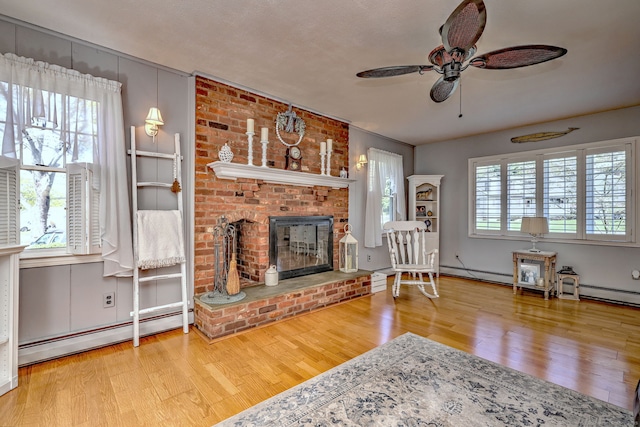 living area with baseboard heating, a brick fireplace, a ceiling fan, wood finished floors, and a baseboard heating unit