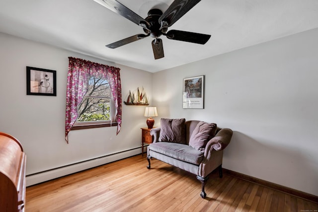 sitting room with a baseboard heating unit, wood-type flooring, a ceiling fan, and baseboards