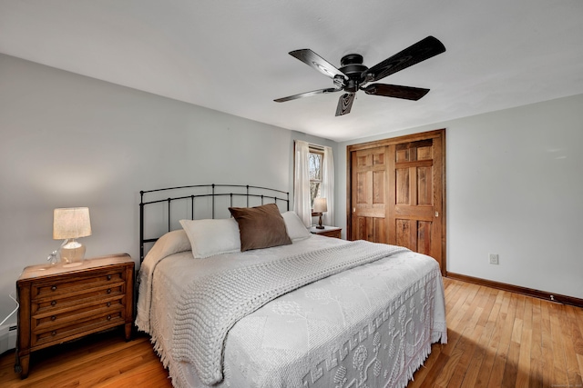 bedroom featuring a closet, baseboards, a baseboard heating unit, a ceiling fan, and hardwood / wood-style floors