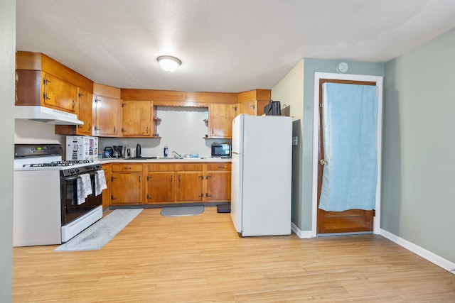 kitchen featuring black microwave, light countertops, freestanding refrigerator, gas range, and under cabinet range hood