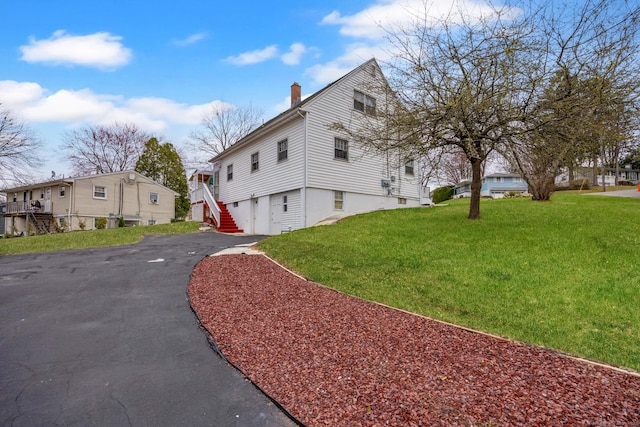 view of property exterior with an attached garage, a lawn, driveway, and a chimney