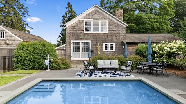 back of property with an outdoor hangout area, a patio area, a fenced in pool, and a chimney