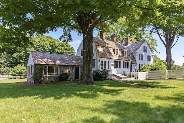 rear view of house with a lawn, a gambrel roof, fence, and a chimney
