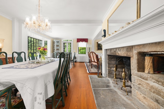 dining room with a fireplace with flush hearth, wood finished floors, an inviting chandelier, and crown molding
