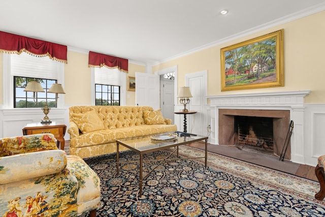 living room with a fireplace with flush hearth, crown molding, wainscoting, wood finished floors, and a decorative wall