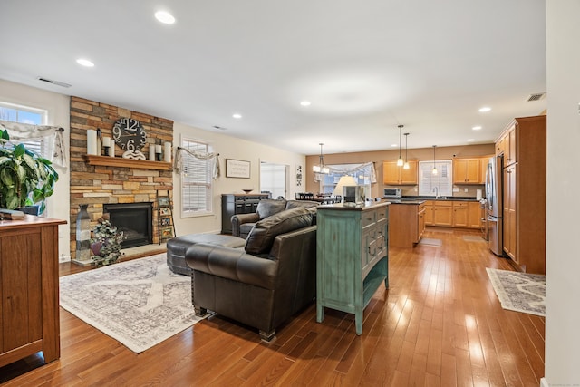 living area featuring plenty of natural light, wood-type flooring, a stone fireplace, and recessed lighting