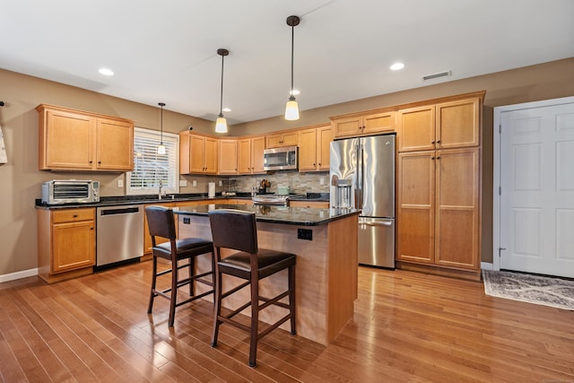 kitchen featuring stainless steel appliances, light wood-type flooring, a center island, a breakfast bar, and hanging light fixtures