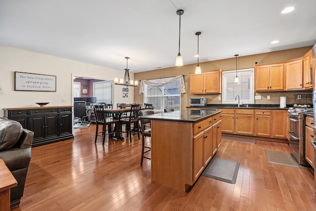 kitchen with range with two ovens, a sink, light wood-style floors, a kitchen bar, and recessed lighting