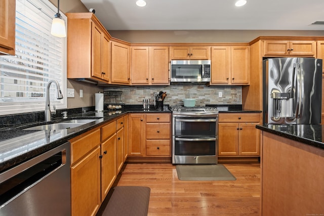 kitchen with appliances with stainless steel finishes, a sink, light wood-type flooring, recessed lighting, and dark stone counters