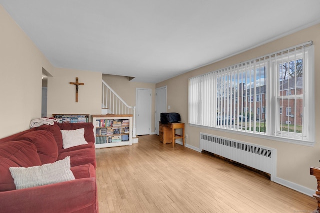 living area with radiator heating unit, a wealth of natural light, wood-type flooring, and baseboards