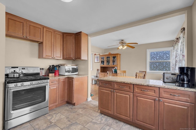 kitchen with light stone countertops, white microwave, brown cabinetry, and gas stove