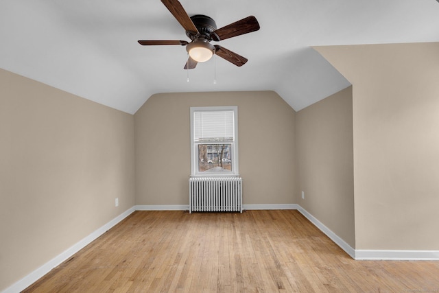 additional living space featuring baseboards, a ceiling fan, light wood finished floors, radiator, and vaulted ceiling