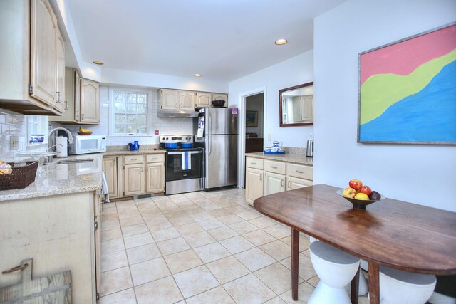 kitchen featuring tasteful backsplash, light tile patterned floors, under cabinet range hood, appliances with stainless steel finishes, and a sink