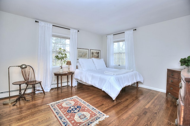 bedroom featuring a baseboard radiator, wood finished floors, and multiple windows