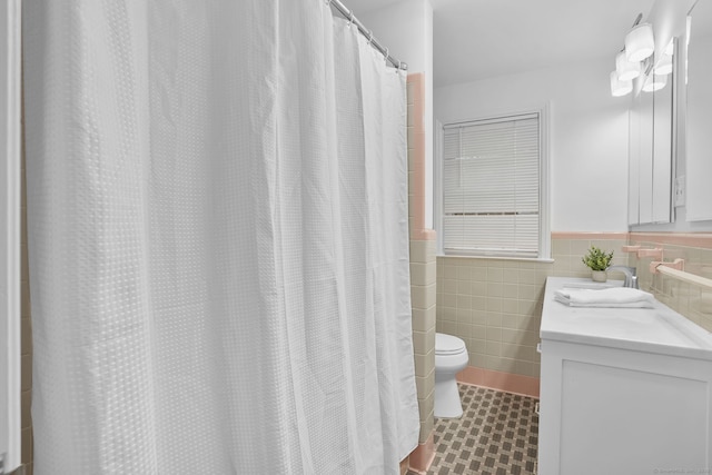 full bath with tile walls, toilet, vanity, and a wainscoted wall