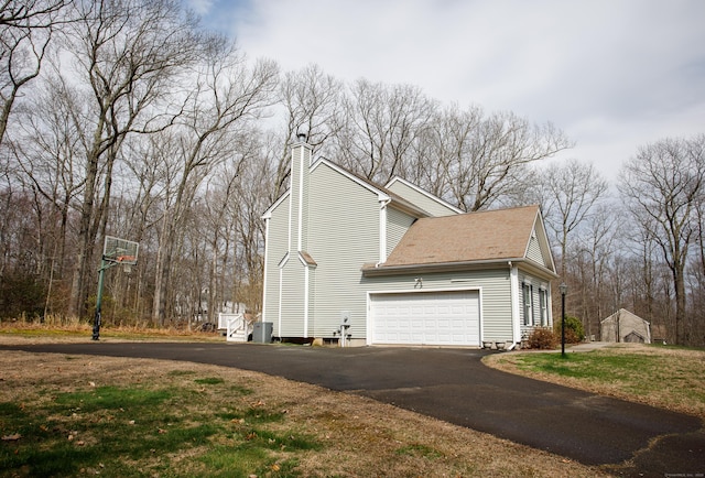 view of side of home with a shingled roof, a yard, driveway, a chimney, and an attached garage