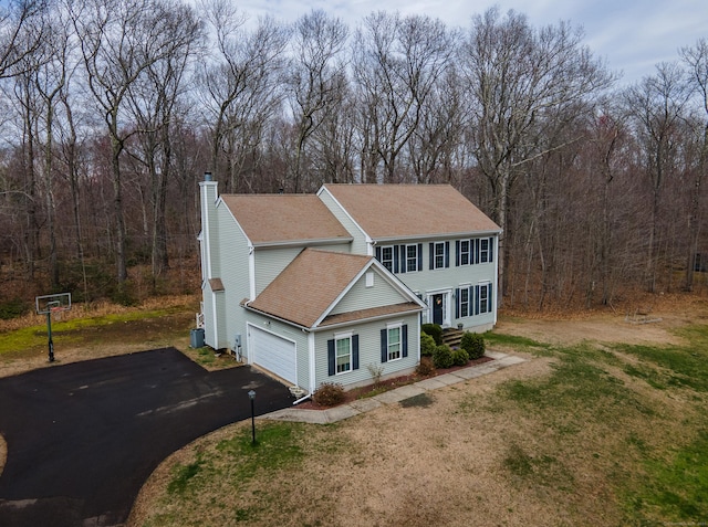 view of front of property featuring aphalt driveway, a chimney, a shingled roof, a front yard, and a garage