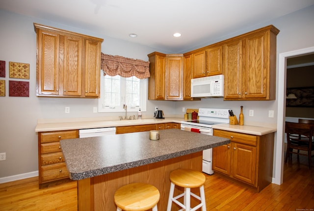 kitchen with a kitchen breakfast bar, a sink, light wood-style floors, a kitchen island, and white appliances