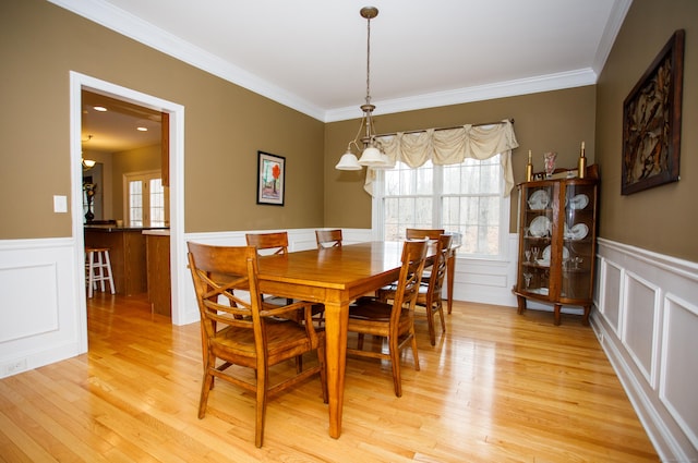 dining space featuring ornamental molding, light wood-style flooring, and wainscoting