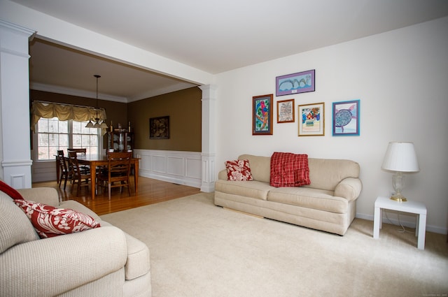 living room featuring a chandelier, ornate columns, ornamental molding, wainscoting, and carpet floors
