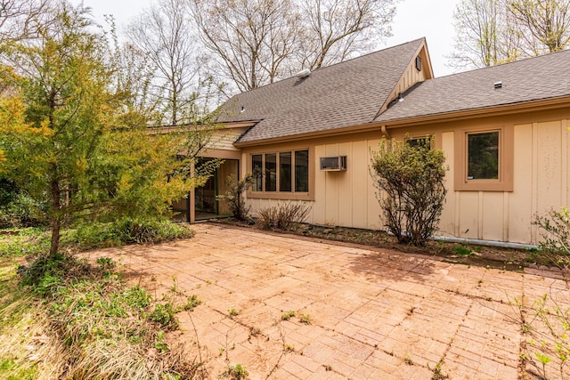 rear view of house featuring a patio, board and batten siding, a shingled roof, and a wall unit AC