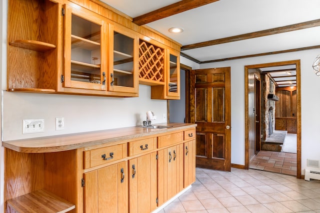 kitchen featuring light tile patterned floors, beamed ceiling, glass insert cabinets, a sink, and light countertops