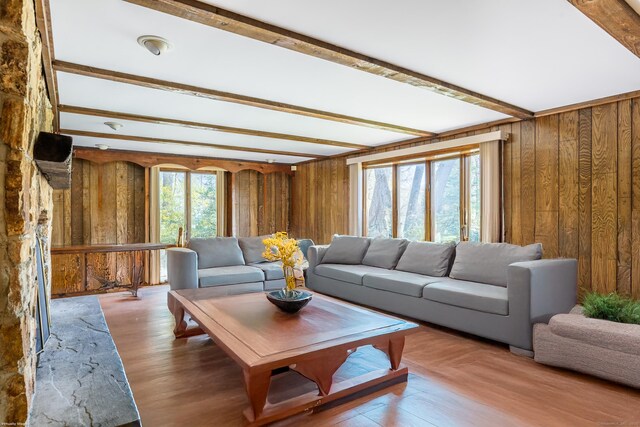living room featuring wooden walls, beam ceiling, and wood finished floors