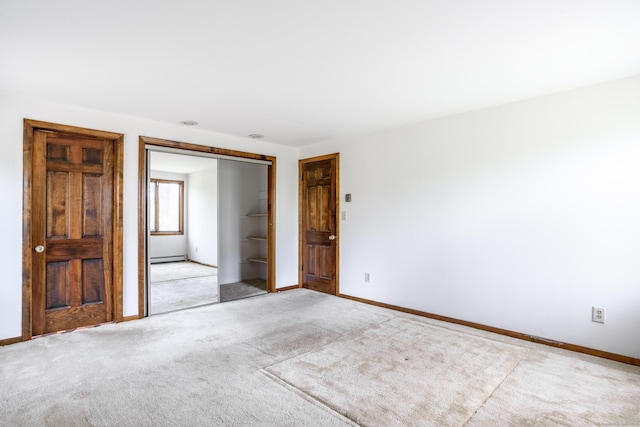 empty room with a baseboard heating unit, light carpet, and baseboards