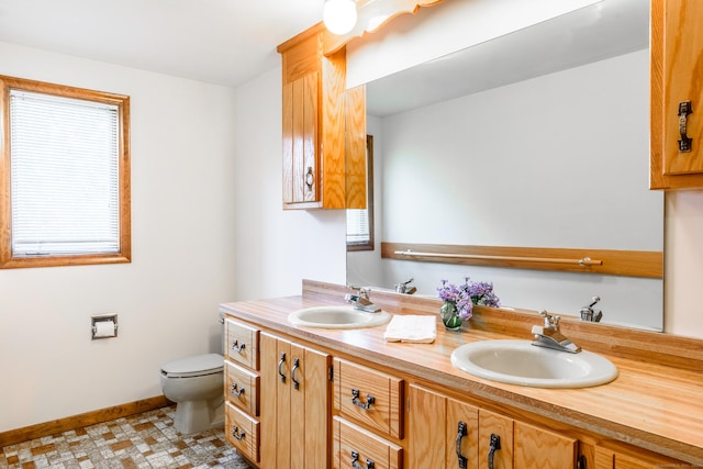 bathroom featuring toilet, double vanity, a sink, and baseboards