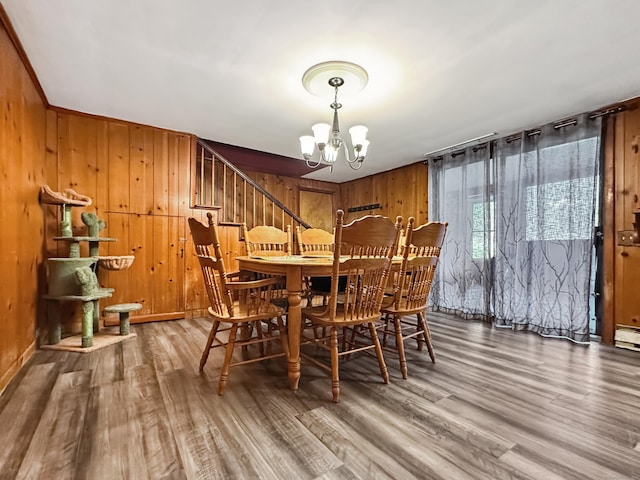 dining room with stairs, wood walls, an inviting chandelier, and wood finished floors