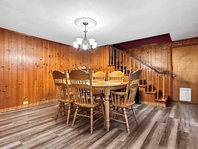 dining area with wooden walls, stairs, wood finished floors, and a notable chandelier