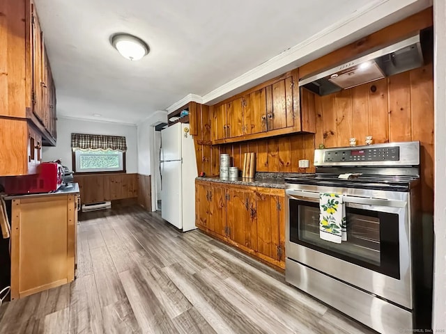 kitchen featuring freestanding refrigerator, brown cabinetry, wall chimney range hood, and electric stove