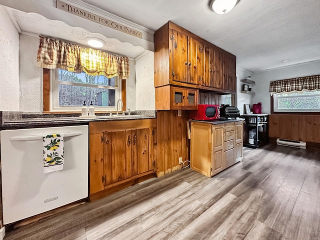 kitchen with white dishwasher, a sink, baseboard heating, light wood finished floors, and brown cabinetry