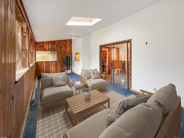 carpeted living area with ceiling fan, wooden walls, and a skylight