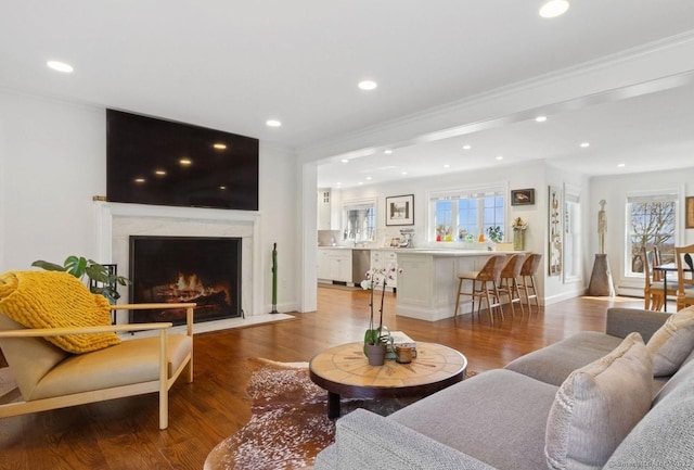living room with wood finished floors, recessed lighting, healthy amount of natural light, ornamental molding, and a premium fireplace