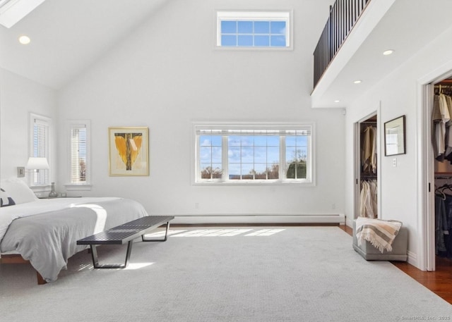 bedroom with high vaulted ceiling, a spacious closet, baseboard heating, a closet, and a skylight