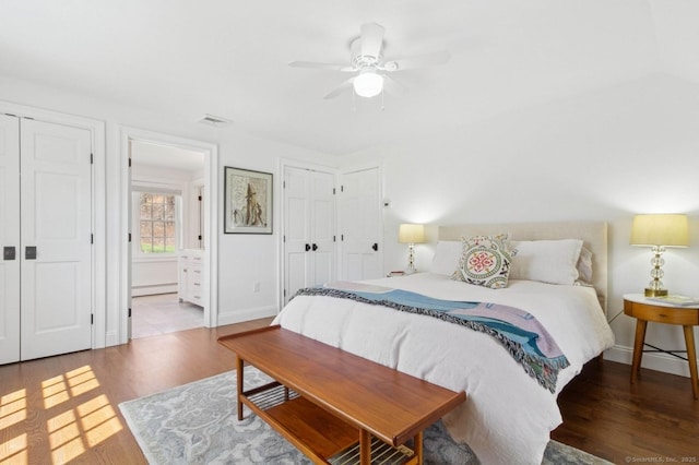 bedroom featuring wood finished floors, a baseboard heating unit, ensuite bathroom, and baseboards