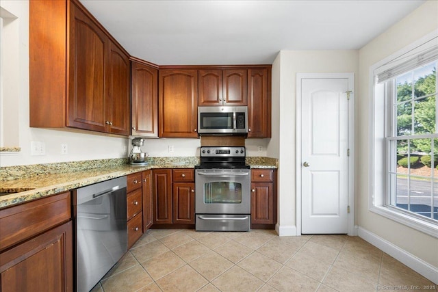 kitchen with light stone counters, brown cabinetry, light tile patterned flooring, stainless steel appliances, and baseboards