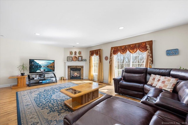 living room with recessed lighting, a warm lit fireplace, wood finished floors, and baseboards
