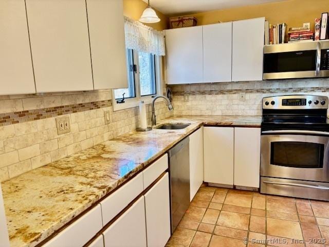 kitchen with light stone counters, white cabinetry, backsplash, appliances with stainless steel finishes, and a sink