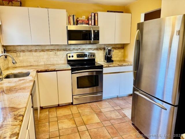 kitchen with a sink, white cabinets, tasteful backsplash, and stainless steel appliances